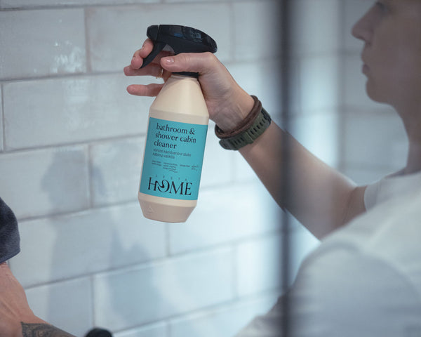Person holding a bottle of 'HOME' body wash in a bathroom setting