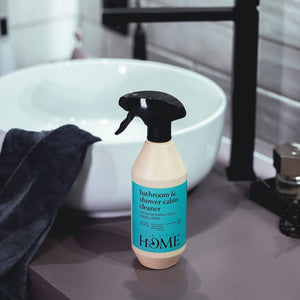 Bottle of bathroom and shower cabin cleaner on a bathroom counter with a sink in the background.