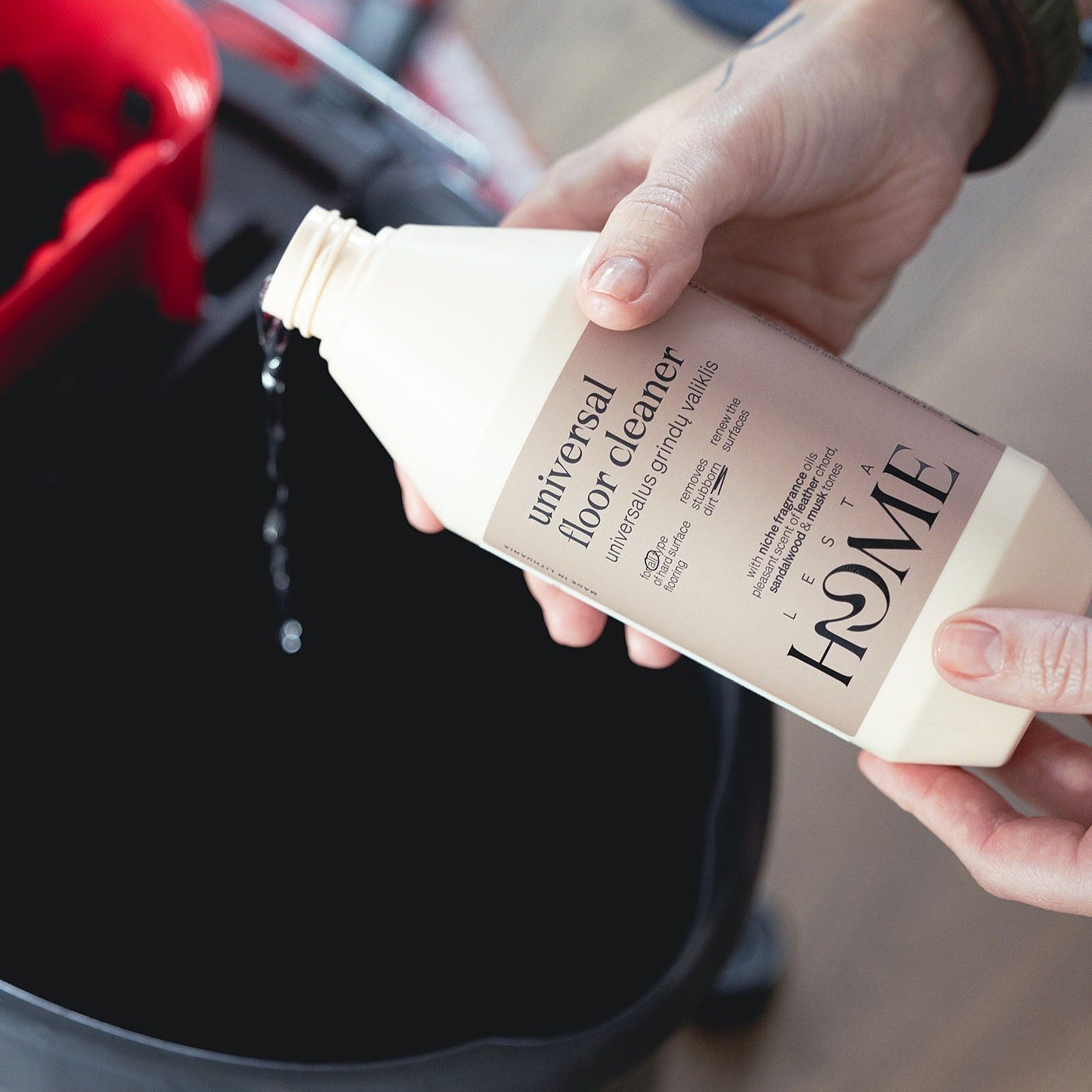 Hand holding a bottle of 'A Home' universal floor cleaner over a black bucket.